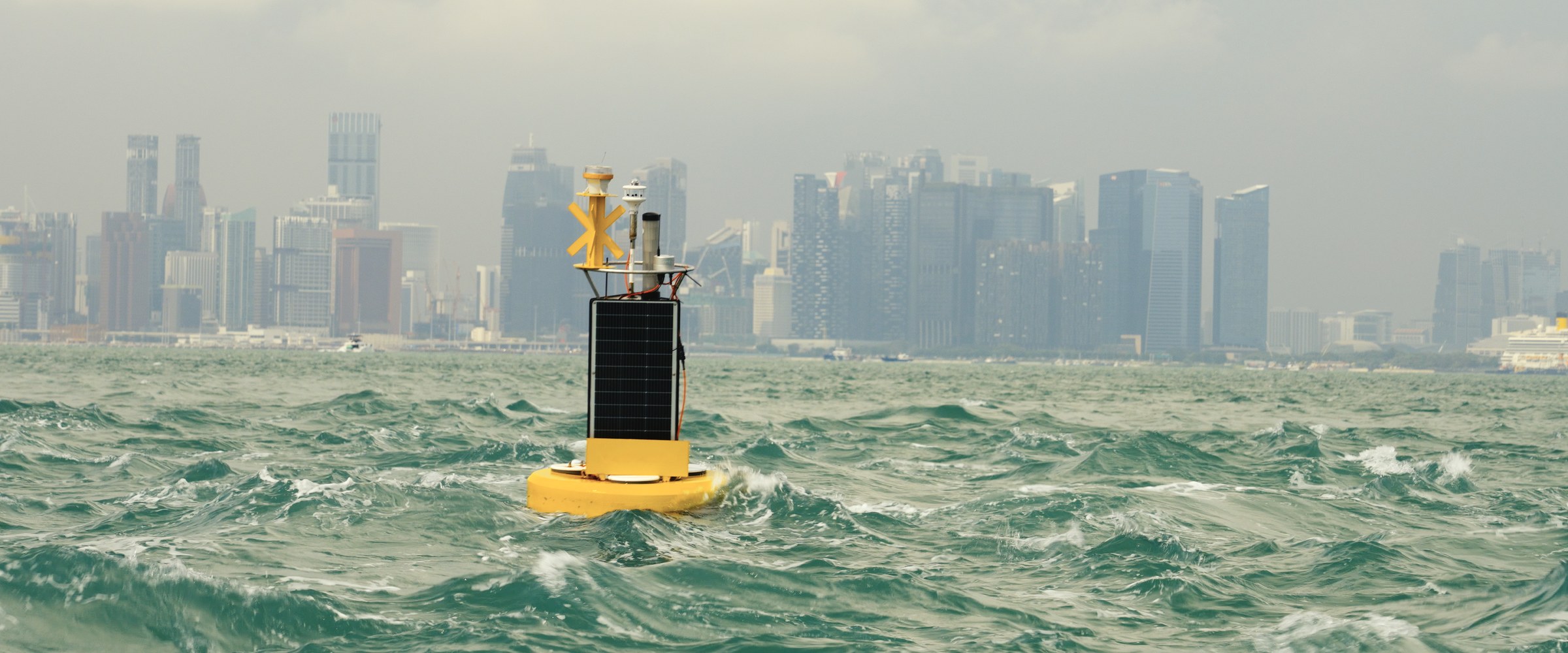 A NexSens data buoy fitted with a Gill weather station in open water, with a city skyline behind.