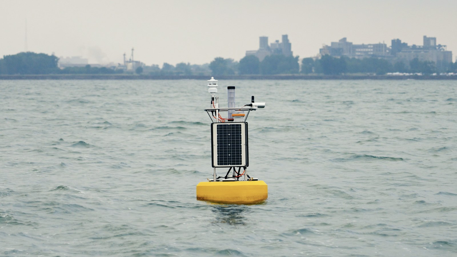 A NexSens data buoy carrying a Gill weather station on open water, with a shoreline behind.